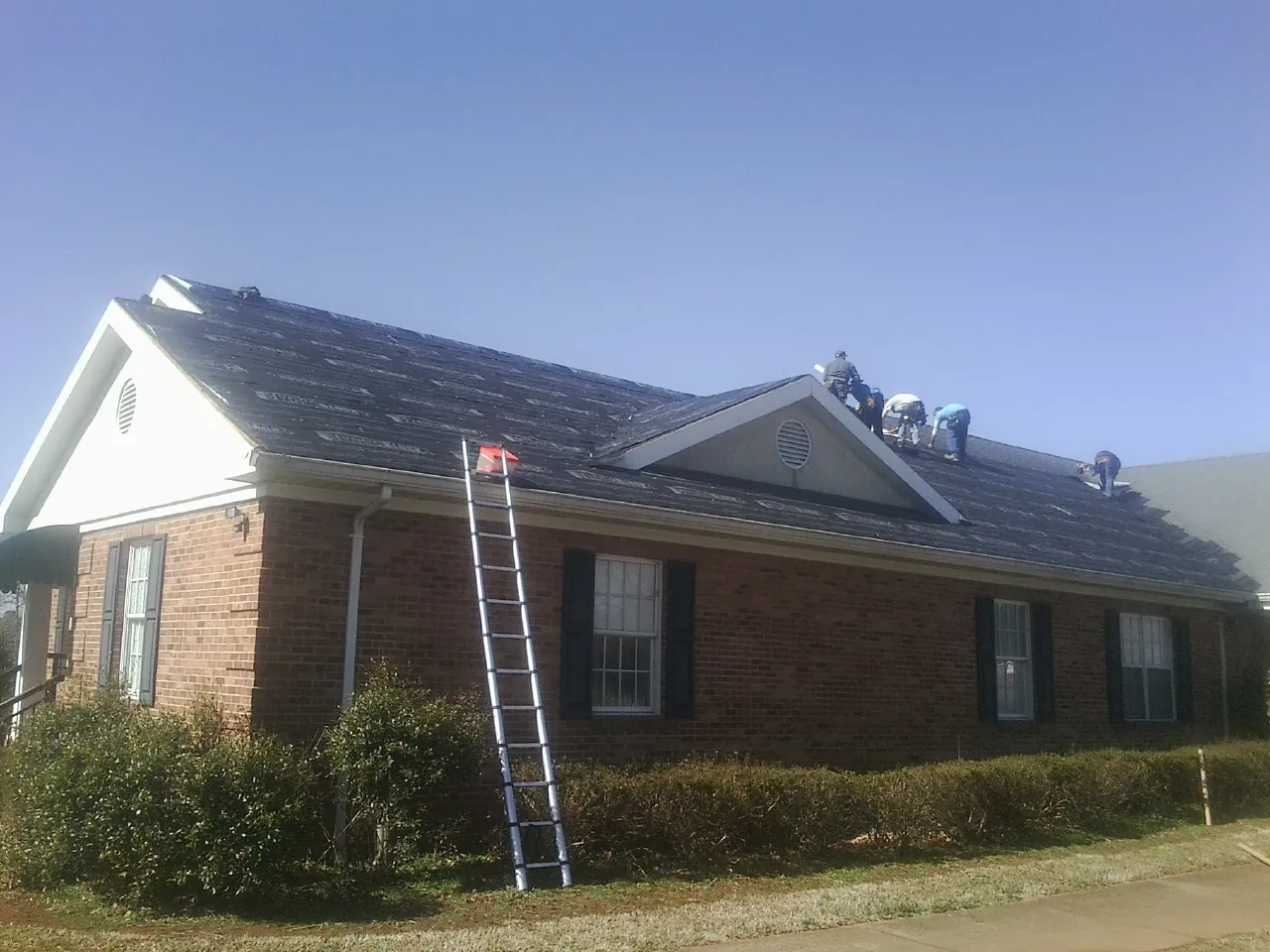 Crew tearing shingles off a brick ranch roof with a ladder set — Metal Roof Repair work by our crew in Topsham