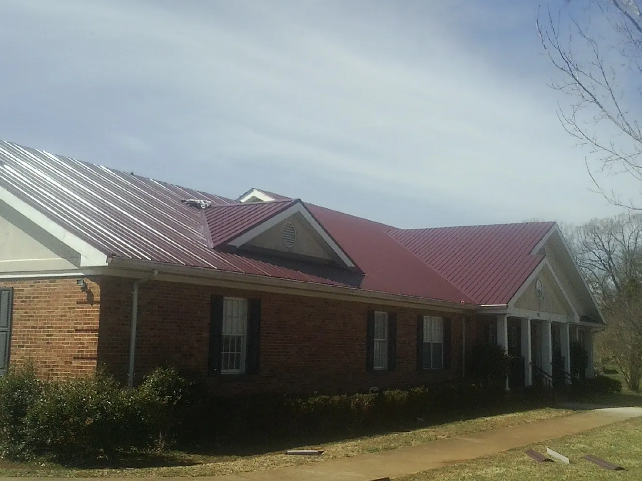 Red metal roof with gabled entries on a long brick building, from a Hail Damage Roof Repair job in Topsham