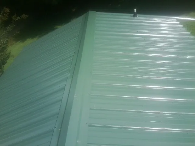 New green metal panels meeting at the ridge of a roof — Flat Roof Repair work by our crew in Topsham
