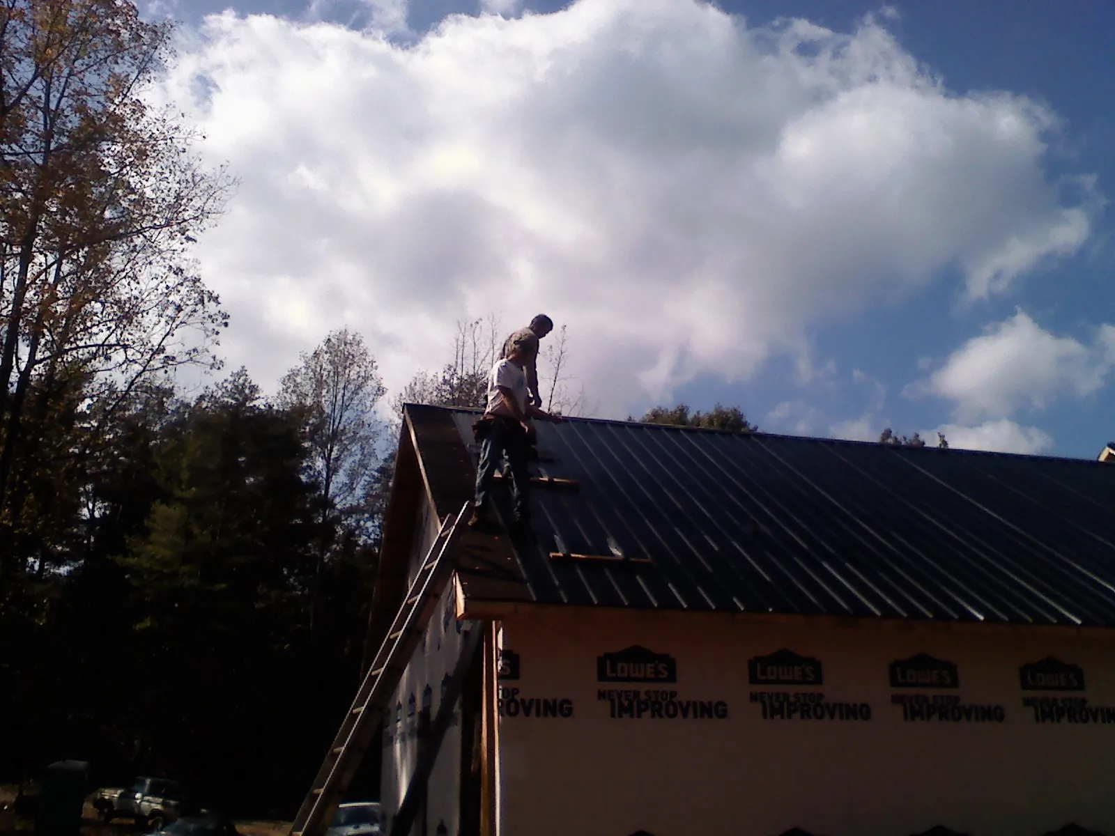 Roofer fastening dark metal panels high against a cloudy sky, from a Roof Inspection job in Topsham