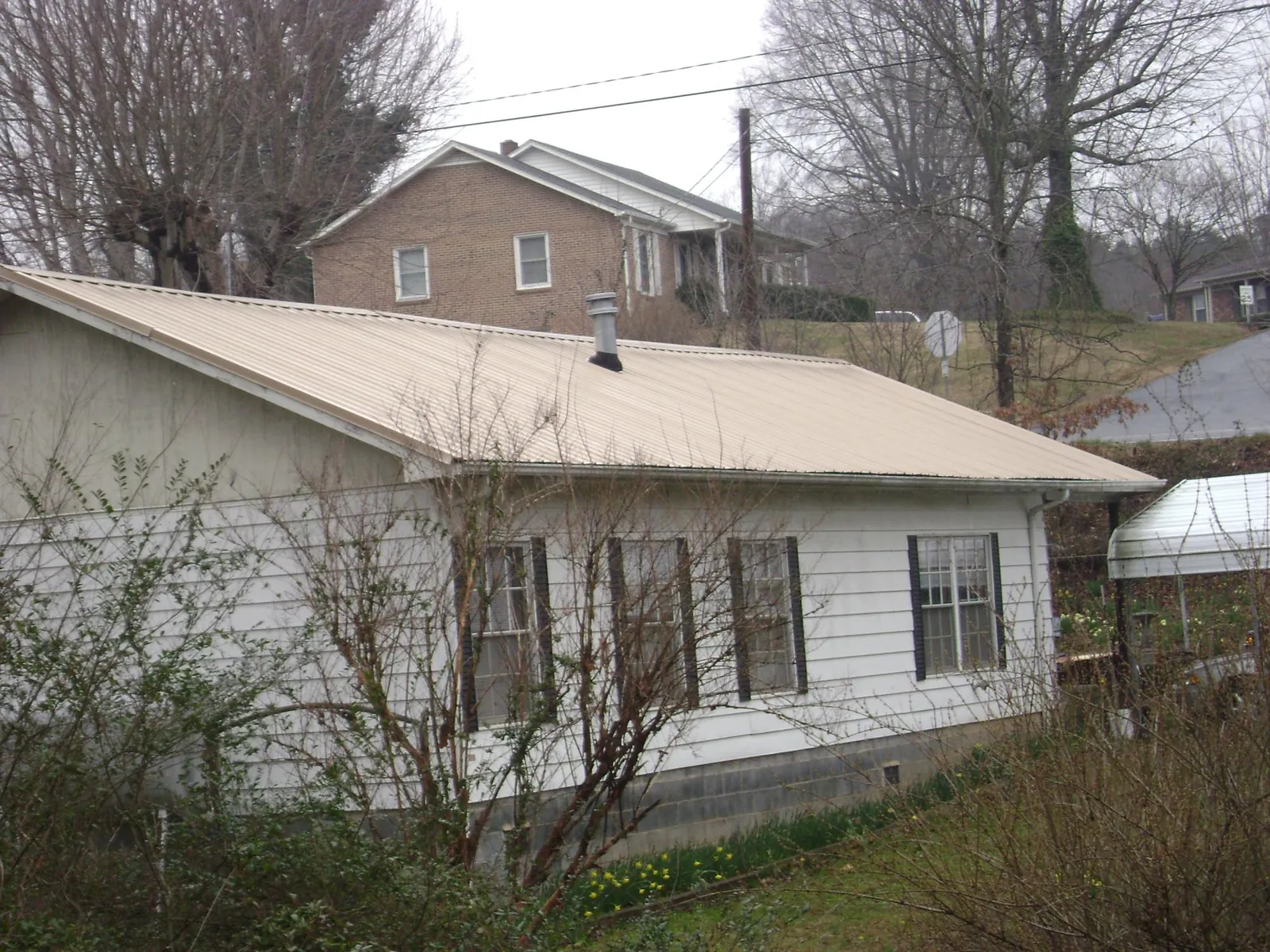 Tan metal roof on a white sided house set into a hillside — Commercial Roofing by Roofing Brothers in Topsham