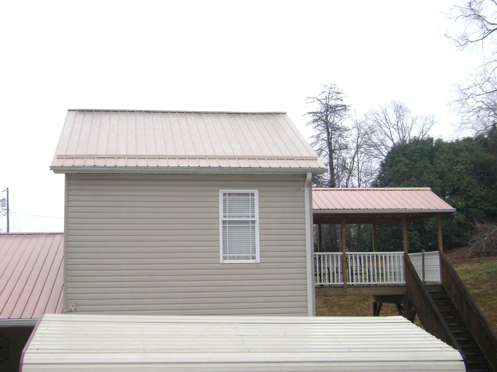 Tan metal roofs on a two story addition and attached porch, from a Roof Replacement job in Topsham